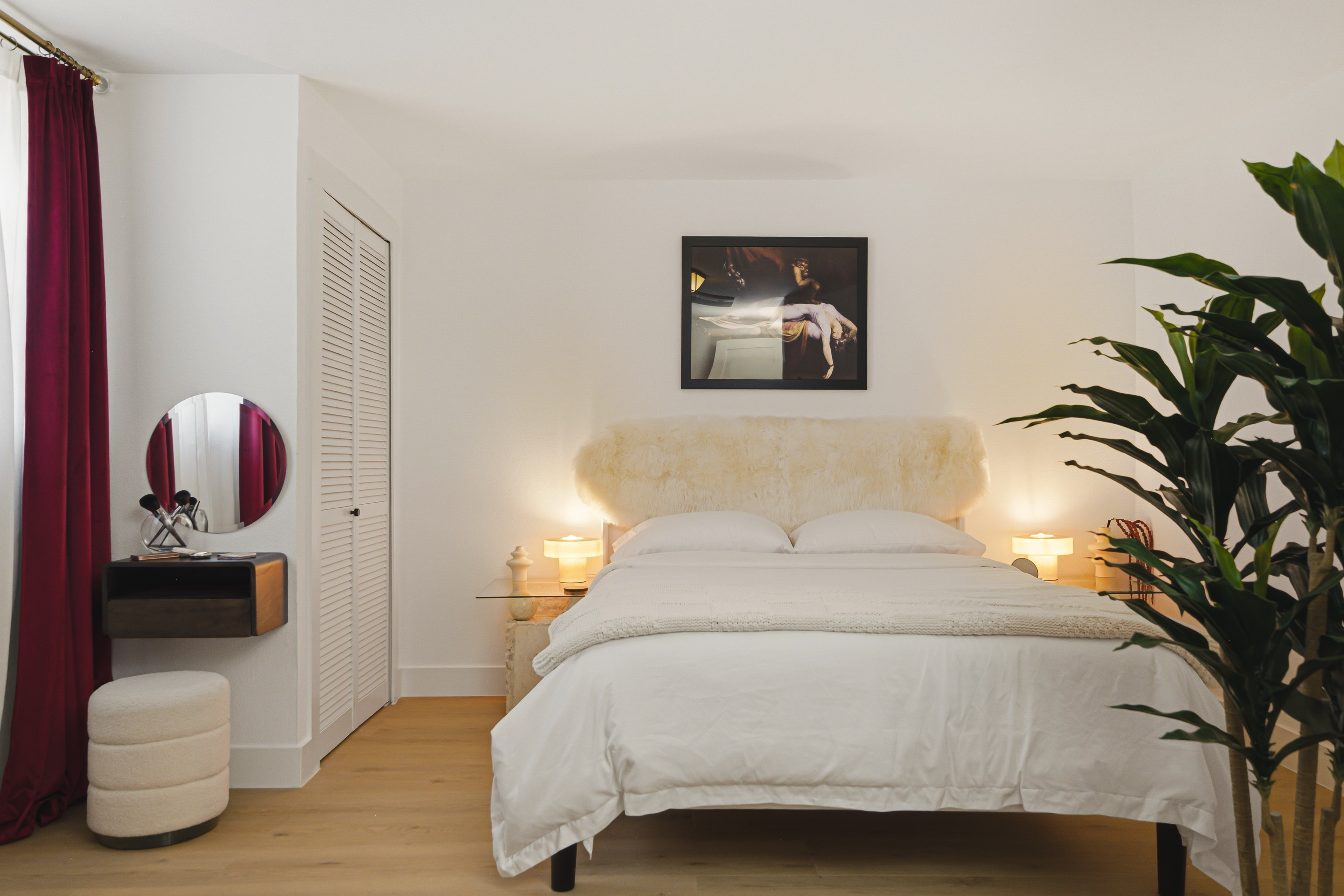 Bedroom with a cream headboard, warm bedside lamps and a round mirror