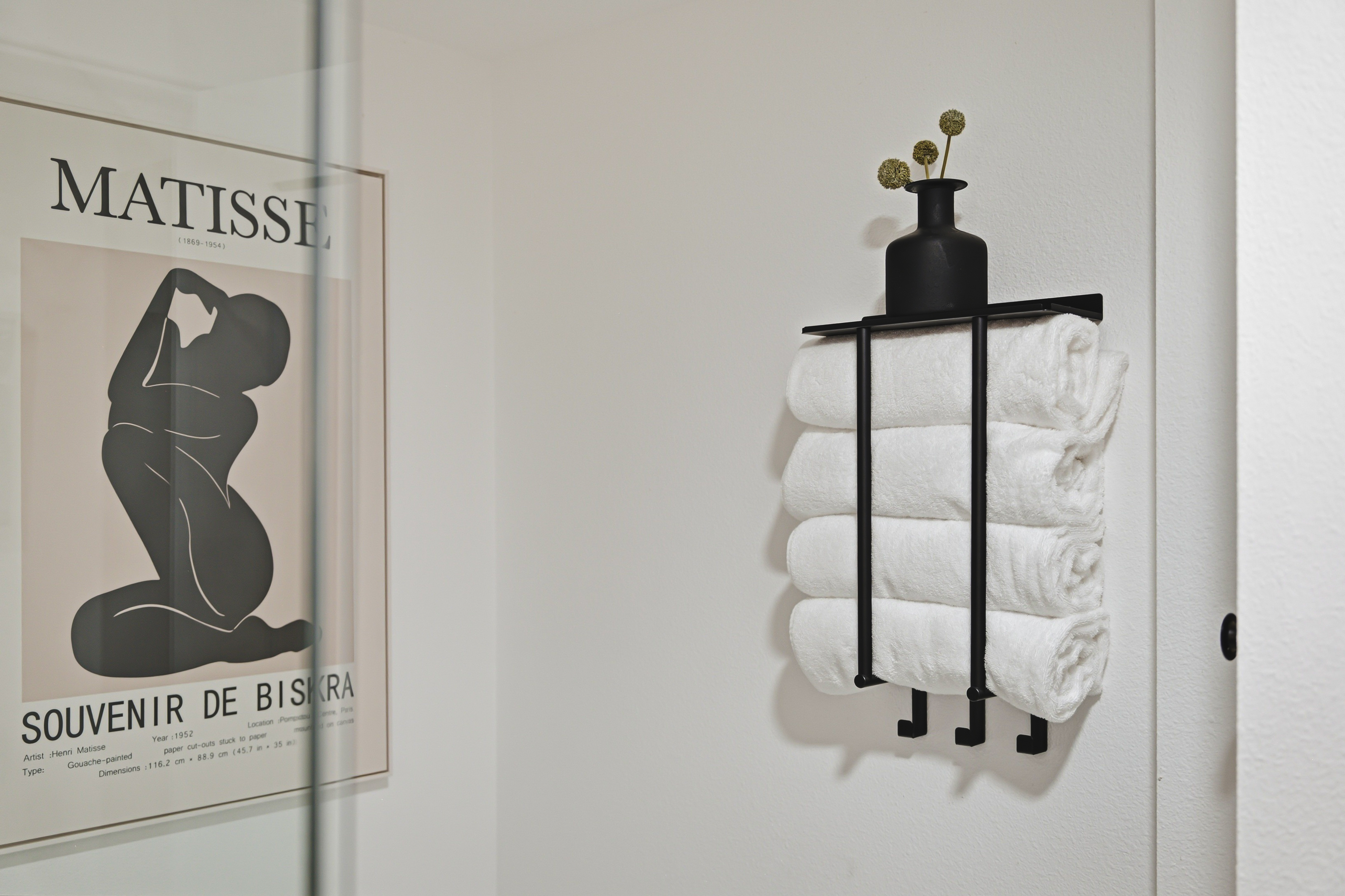 Rolled cotton towels on a wall rack beneath a framed Matisse print