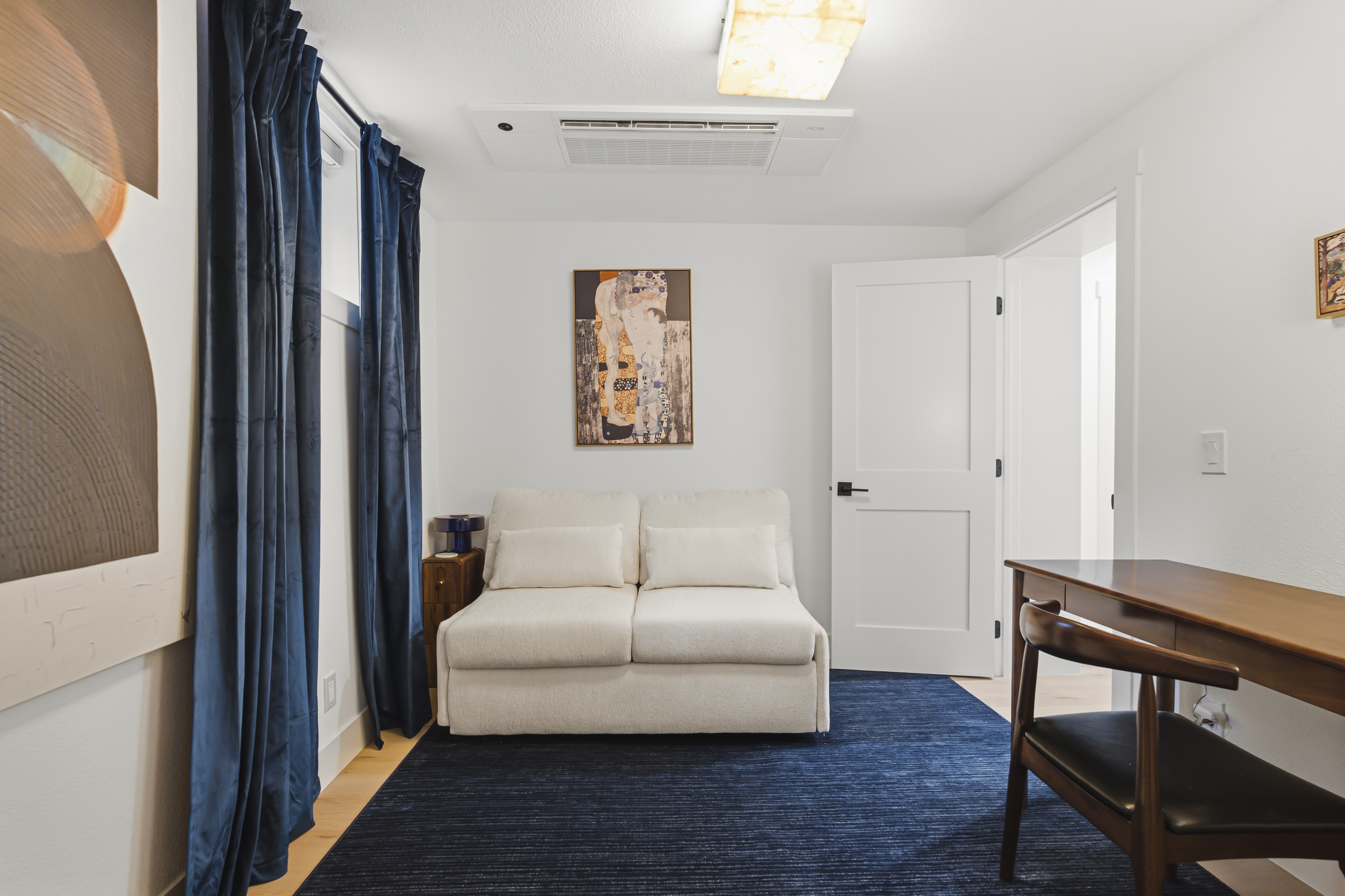 Third room with a sofa bed, navy curtains, blue rug and a desk