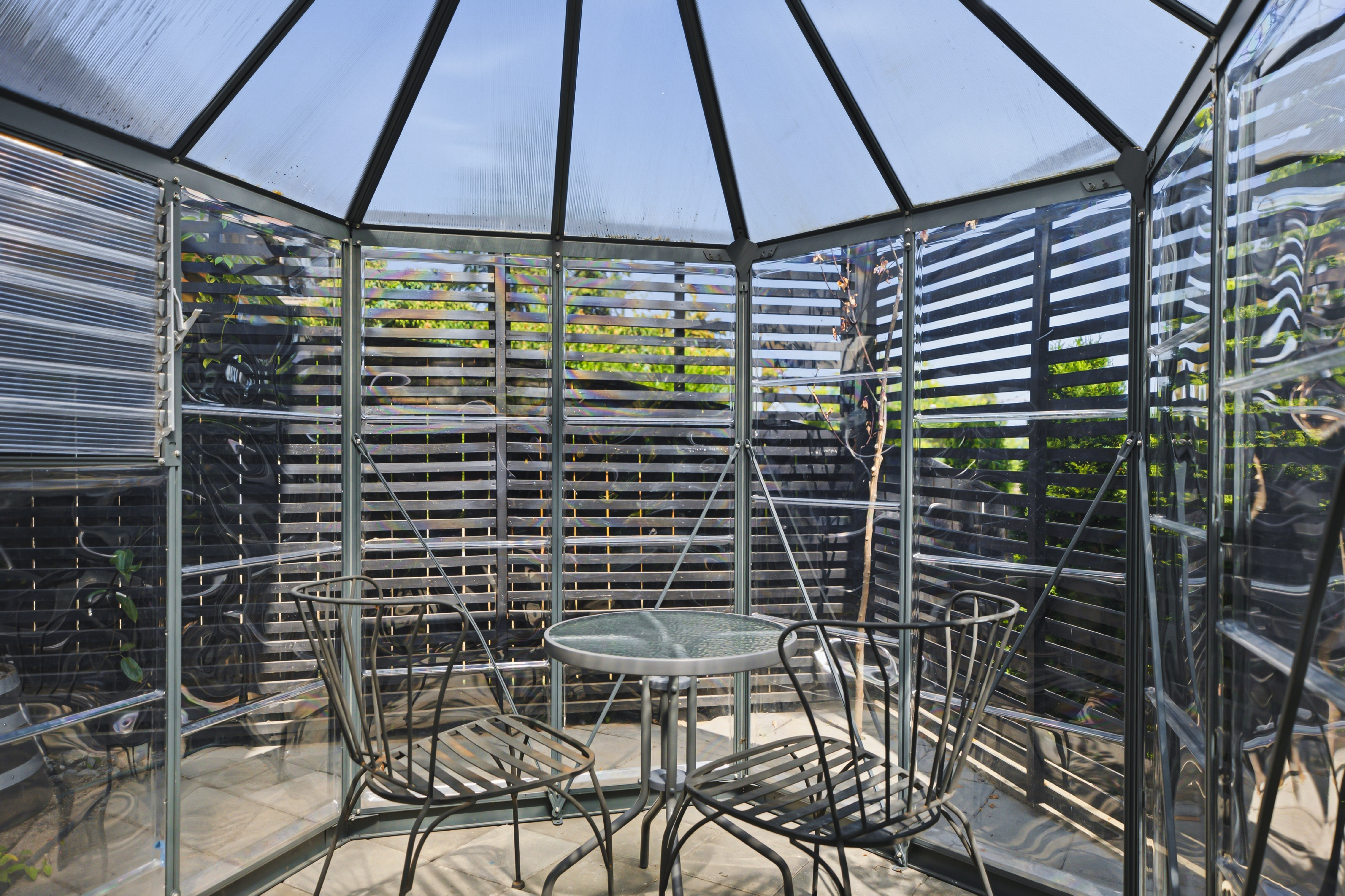 Glass greenhouse in the garden with a small table and chairs